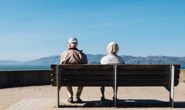 Older couple sitting on a bench facing mountains