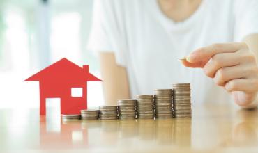 an individual stacking coins next to a small model home