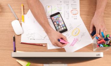 A hand writing on paper on a desk with a phone next to it