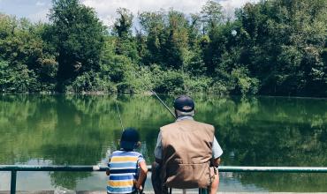 A man and a small boy fishing together seen from the back
