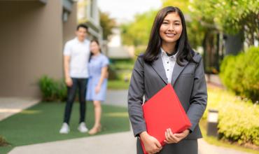 A woman holding a red folder standing in front of a couple that just bought a home