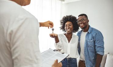 Two people accepting a key for their home from a real estate agent