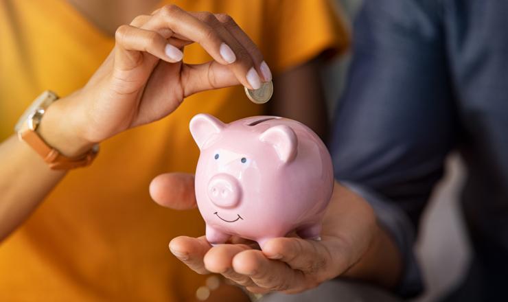 One person holding a piggy bank and another person adding a coin to the top
