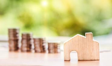 A small wooden house on a table with coins in the background