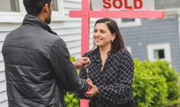 A woman shaking a man's hand in front of a sold sign