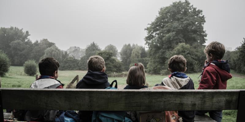 Four children sitting on a bench with their backs to the photographer