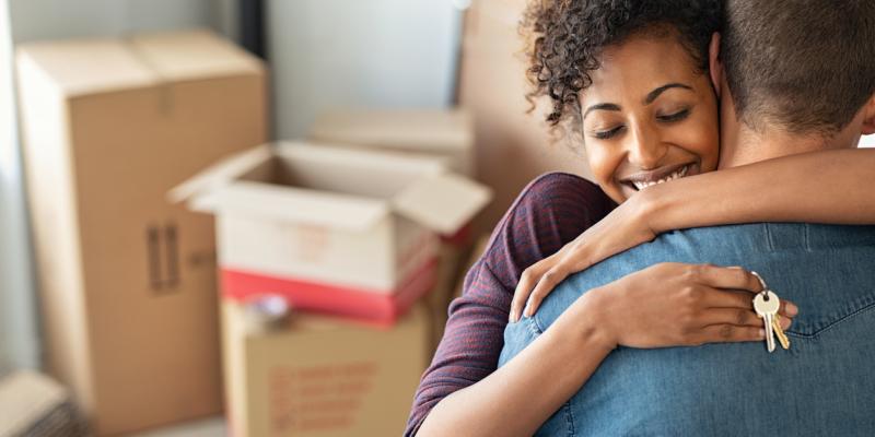 two people hugging in front of moving boxes holding a key