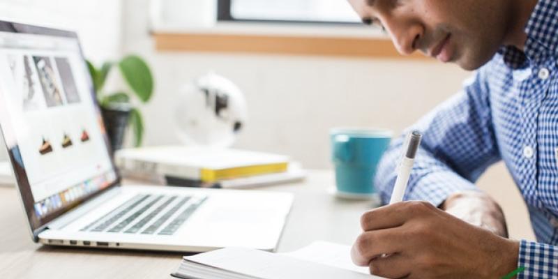 Man sitting in front of computer writing in a journal