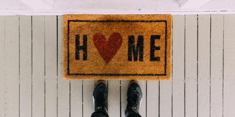 Two feet standing in front of a doormat that says Home