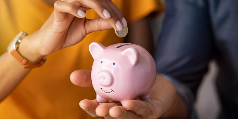 One person holding a piggy bank and another person adding a coin to the top