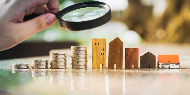 A magnifying glass over a stack of coins and houses