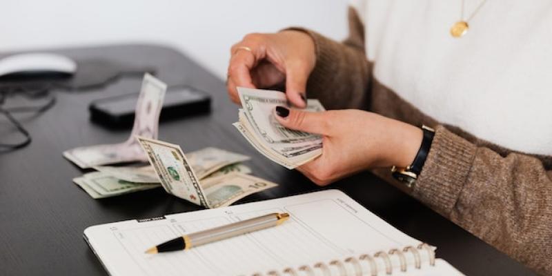 A person counting money on a desk with a notepad in front of them