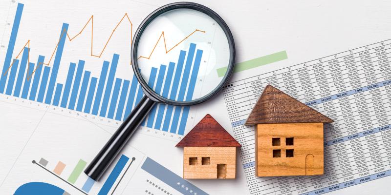 A magnifying glass and small wooden houses laying on paperwork with graphs on it
